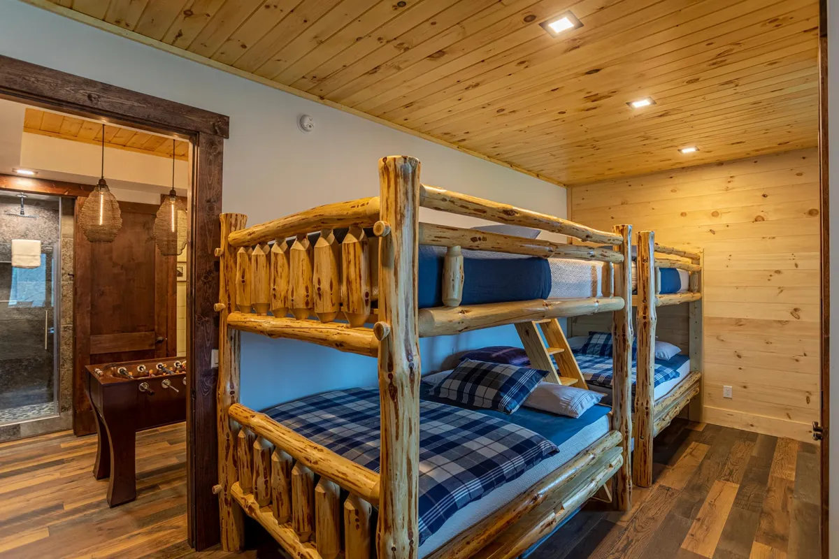 A playful and comfortable bunk room featuring multiple wooden bunk beds and a foosball table, perfect for children or groups. The warm wood tones and casual decor create an inviting and functional space for larger parties or families.