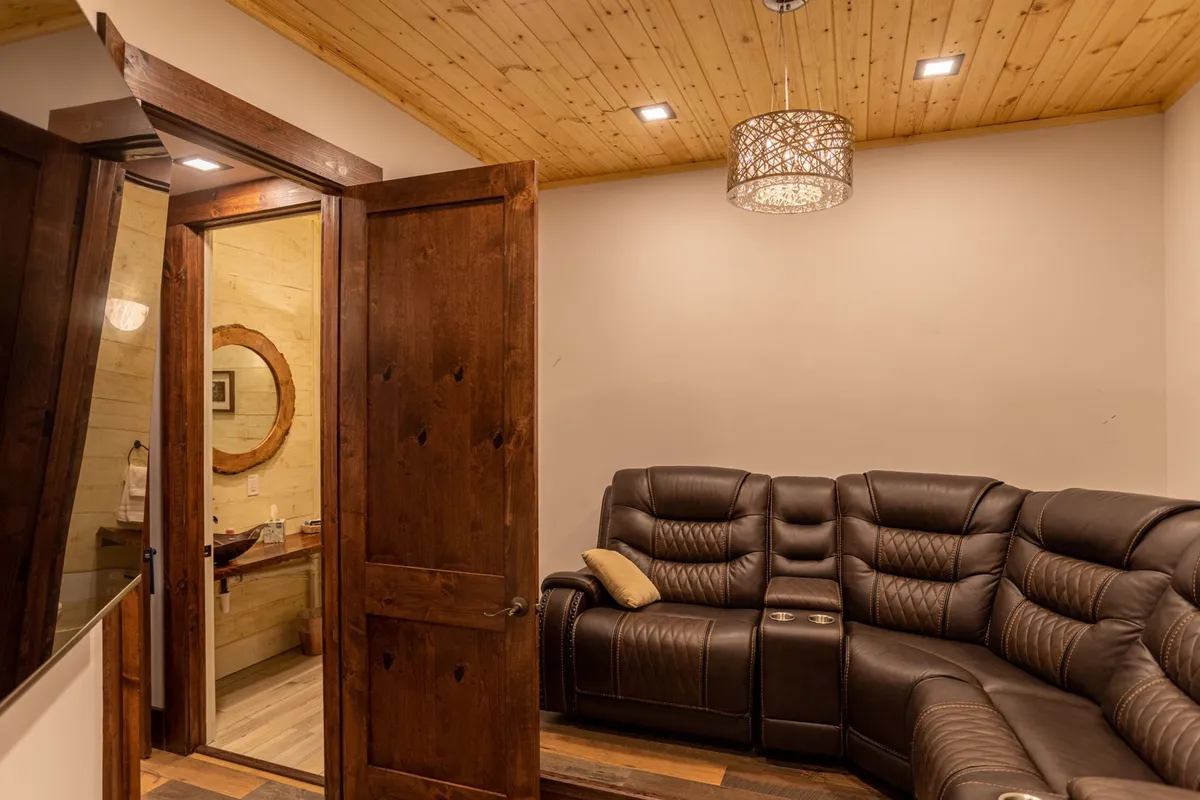 A plush leather sectional faces a large screen in a cozy, softly lit home theater room. Warm wood accents, a ceiling light fixture, and a welcoming layout provide the ideal environment for movie nights, socializing, and relaxation.