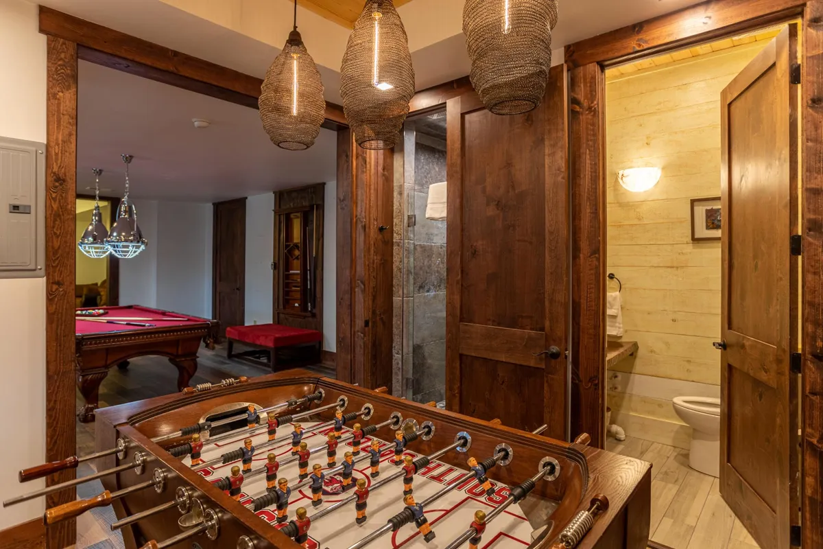 This interior image showcases a vibrant game room featuring a foosball table, pool table, and inviting wooden doors with hanging lights. The casual and fun environment is designed for friendly competitions and social interaction, echoing the section's mention of game tournaments and activities for all ages.