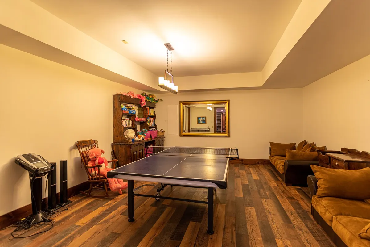 A bright and casual space centered around a ping pong table, accented by a decorative mirror and plush wooden furniture. Stuffed animals lend a family-friendly vibe, while open space invites movement and friendly competitions.