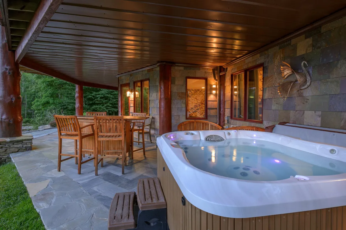 The image shows a bubbling hot tub and an outdoor dining table set amidst the home’s natural surroundings. The scene radiates relaxation and sociability, with the hot tub offering a perfect spot to soak in the views and the table providing space for gatherings under the stars.