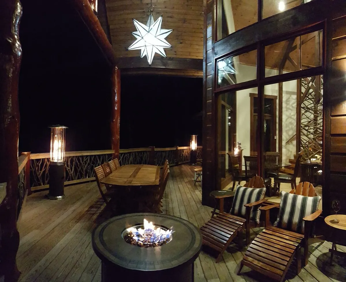 A cozy fire pit area with outdoor seating on a wooden deck, accented by a decorative star light above. Trees enclose the space, creating privacy and an intimate setting perfect for evening gatherings, storytelling, or enjoying a glass of wine by the fire.